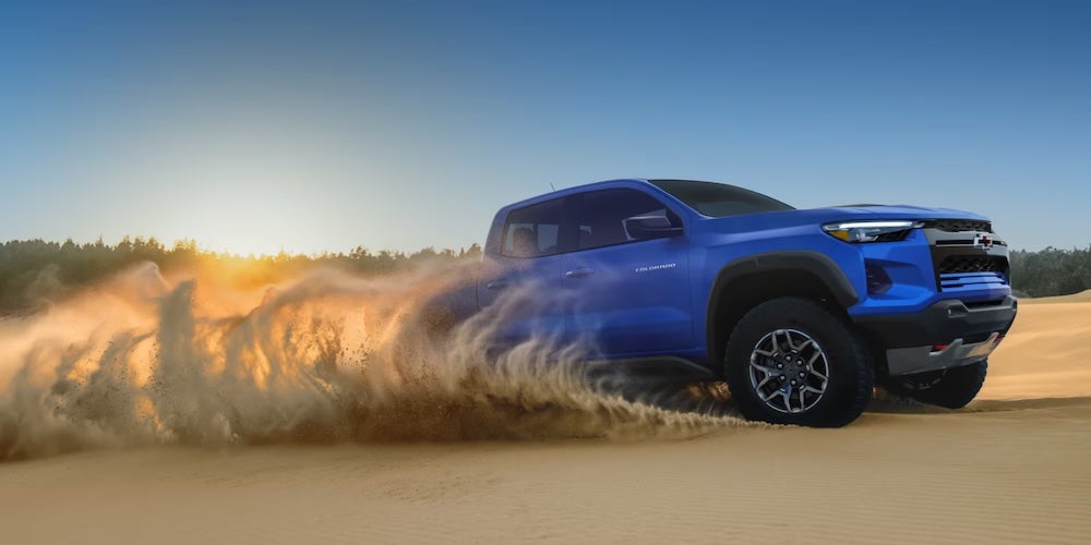 A bright blue 2026 Chevrolet Colorado pickup truck driving up a sand dune