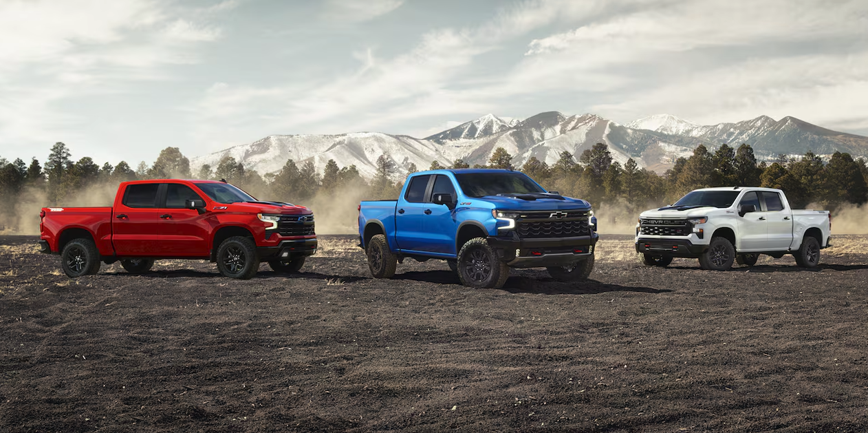 Three 2026 Chevrolet Silverado 1500 trucks parked off-road with mountains in the background
