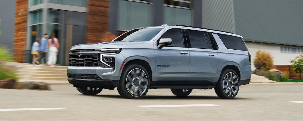 A silver 2026 Chevrolet Suburban SUV driving down a city street