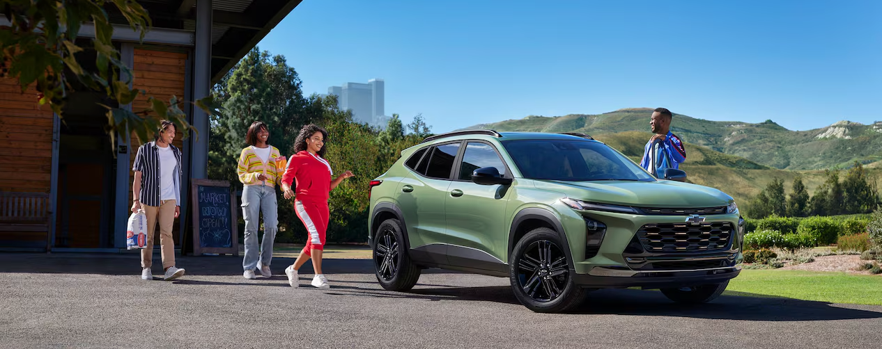 People approaching a green 2026 Chevy Trax on a clear-skied day