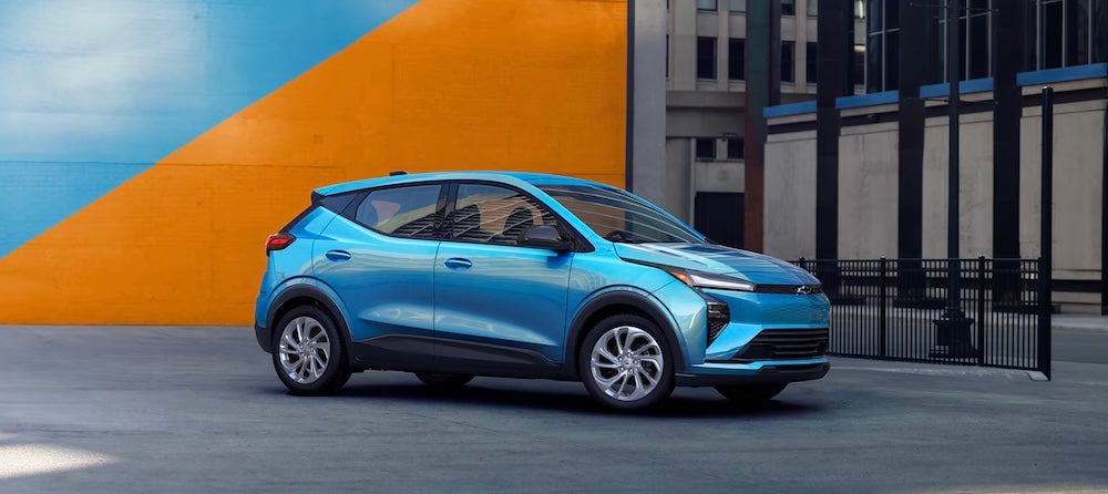 A bright blue 2027 Chevrolet Bolt EV parked in front of an orange and blue wall