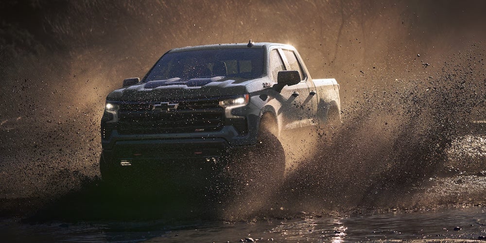 A black Chevrolet Silverado 1500 truck splashing through muddy water