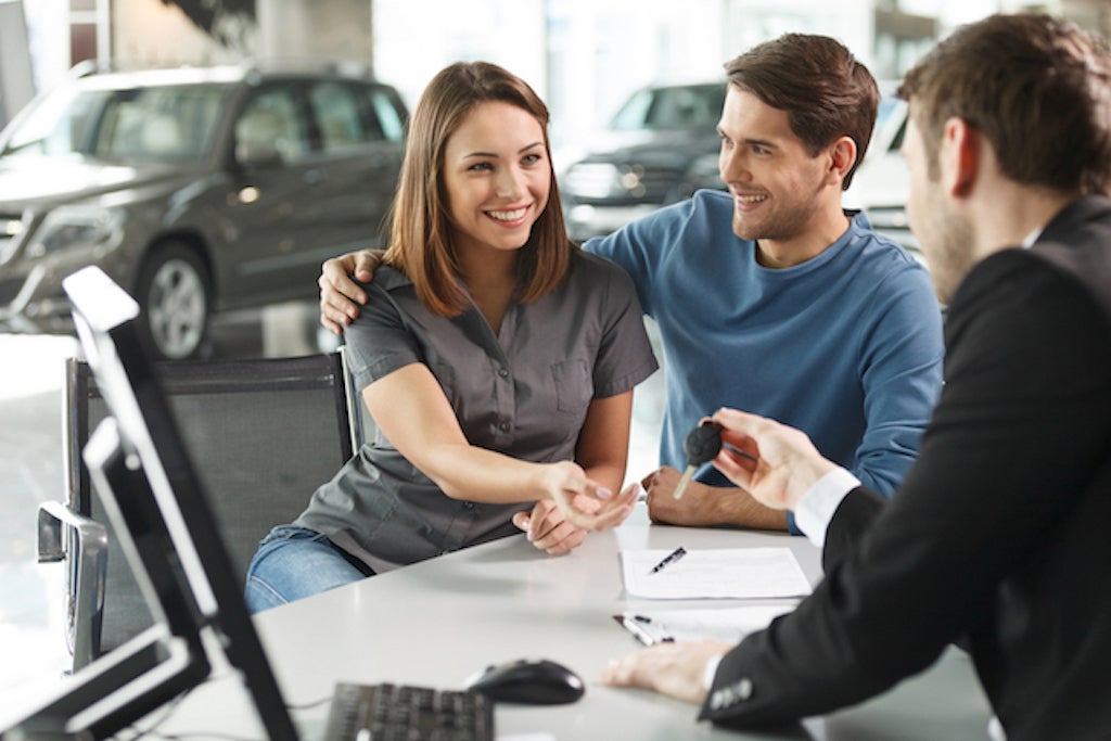 A sales team member giving car keys to a couple at the dealership desk